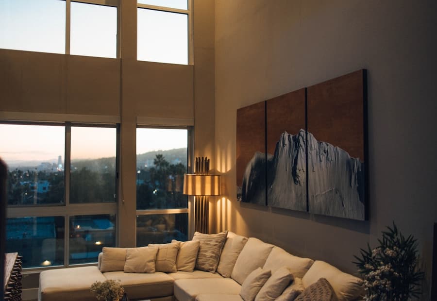 A living room at dusk with a cream sectional and floor-to-ceiling city windows