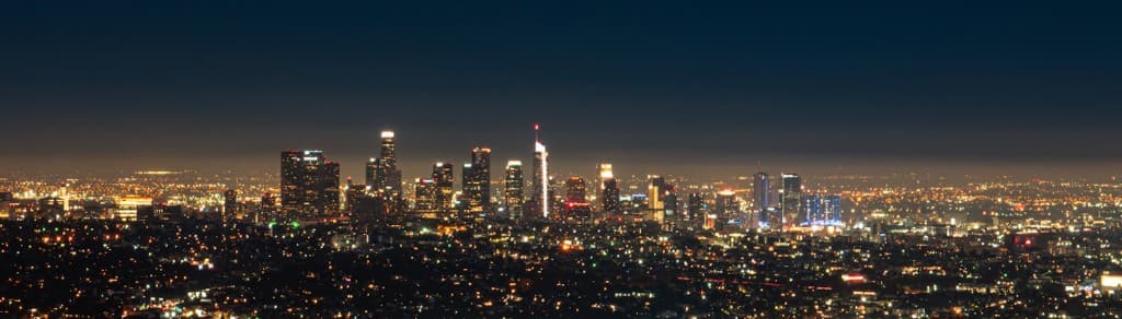 A night cityscape with a skyline of lit towers over a carpet of urban lights